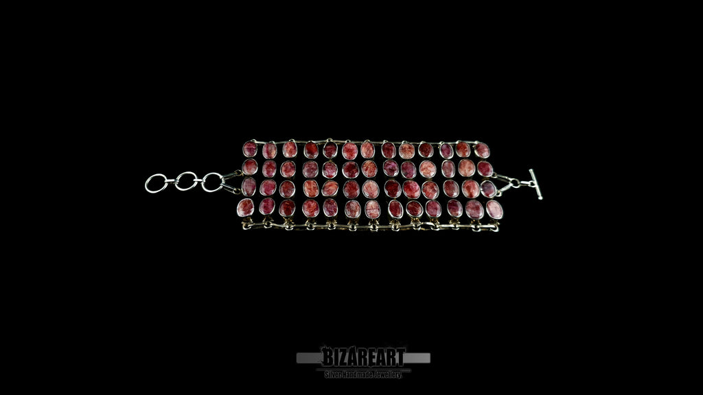 Full horizontal lay out of wide 13-row artisan silver collar necklace with 52 natural ruby stones against black backdrop.