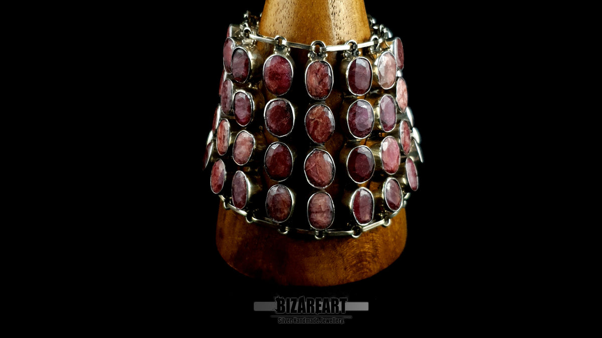 Macro close-up of natural raw ruby gemstones hand-set in sterling silver bezel frames on an articulated matrix collar.