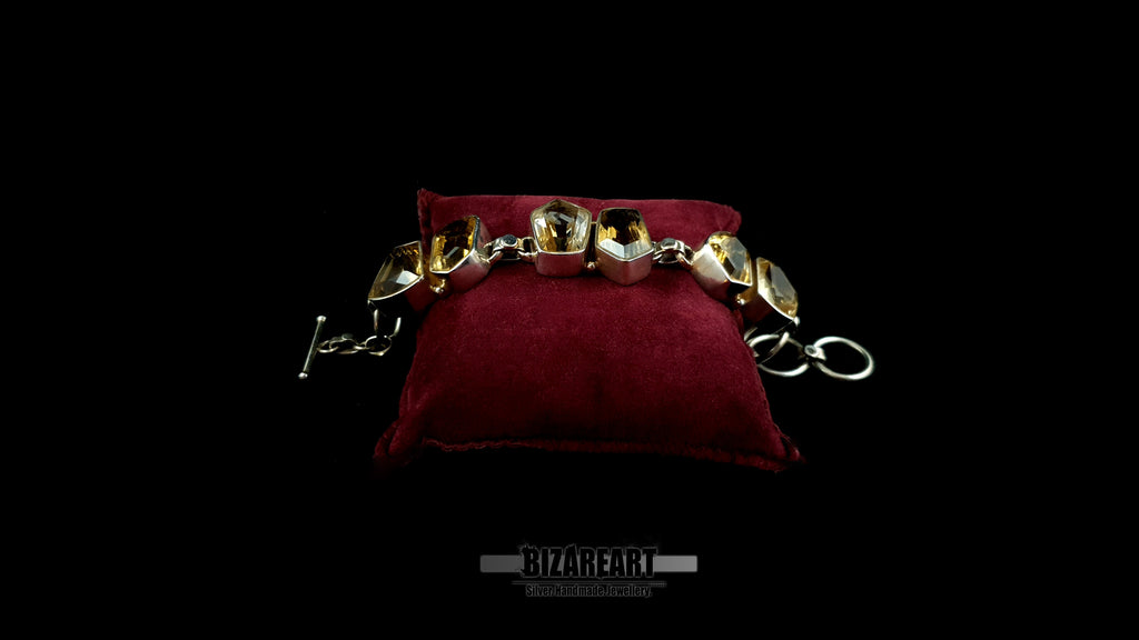 Front profile view of heavy silver statement bracelet with golden citrine stones on red cushion