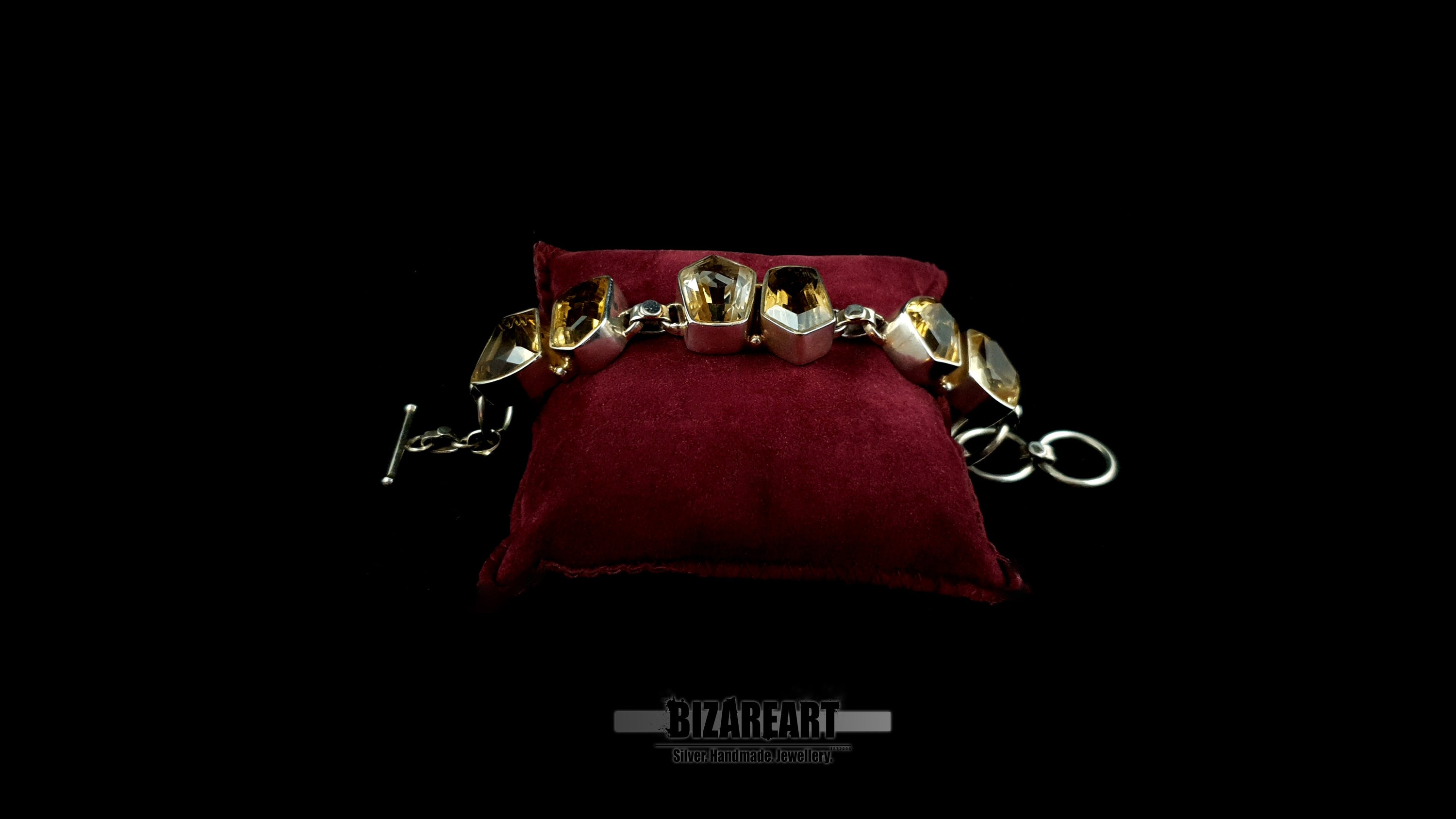 Front profile view of heavy silver statement bracelet with golden citrine stones on red cushion