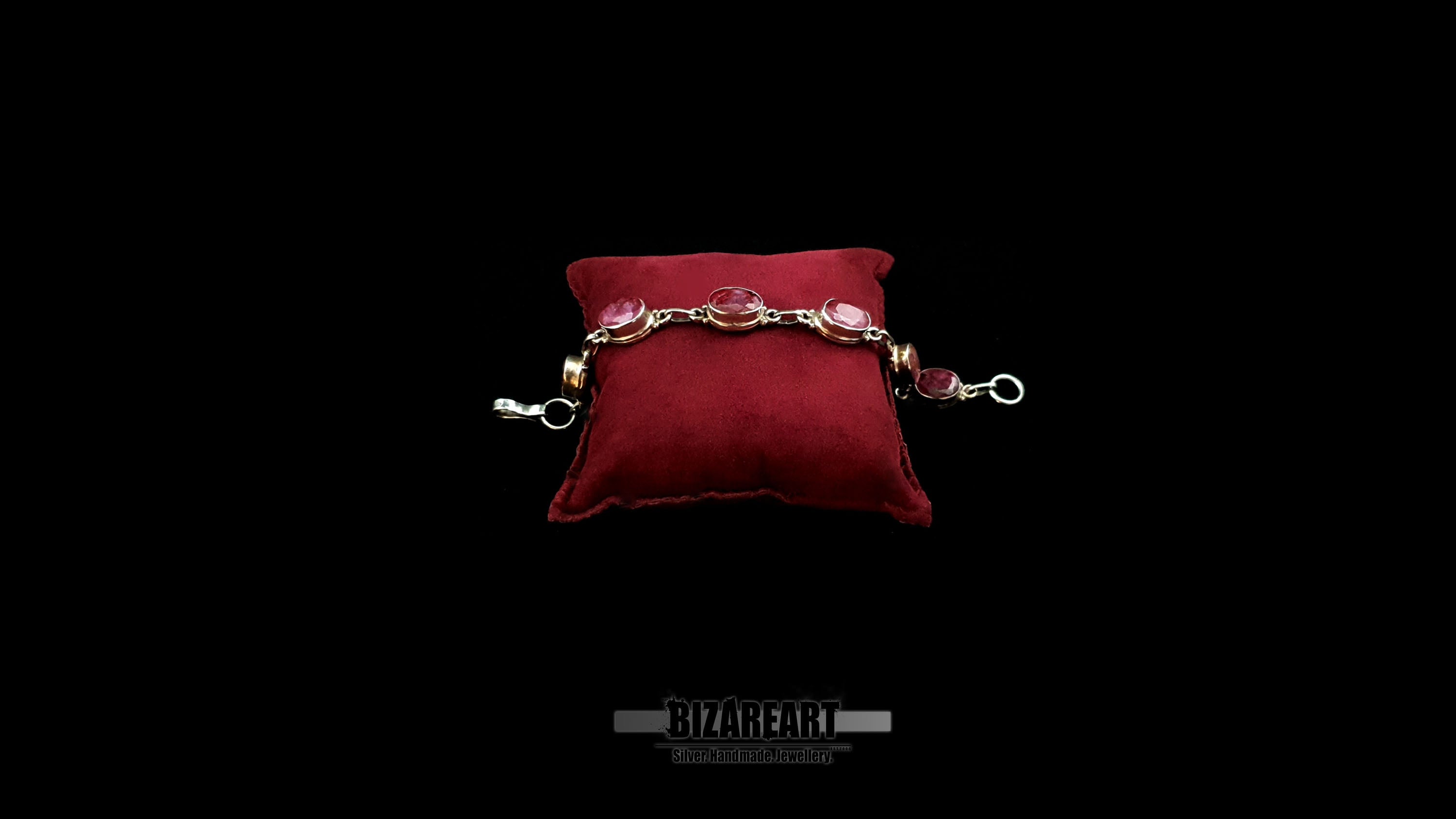 Handmade raw ruby and sterling silver link bracelet resting on a plush crimson velvet display cushion against a solid black background.