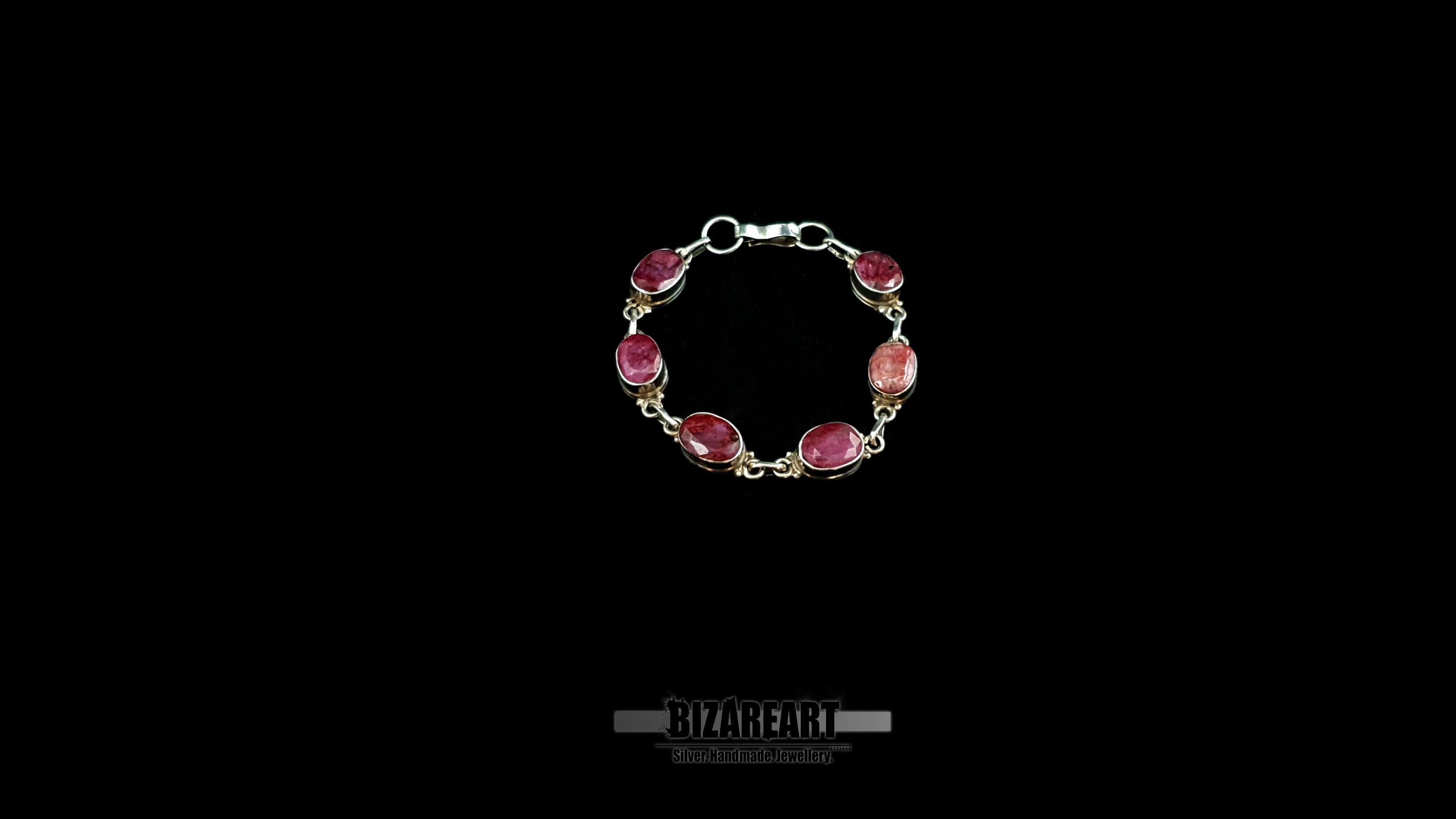 Centered product shot of an open-clasp sterling silver bracelet set with six faceted raw pinkish-red ruby gemstones.