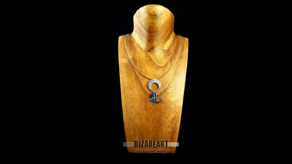The handmade silver whale pendant worn on a silver chain layered on a gold mannequin bust, demonstrating how the kinetic necklace hangs seamlessly and styles with modern fashion.