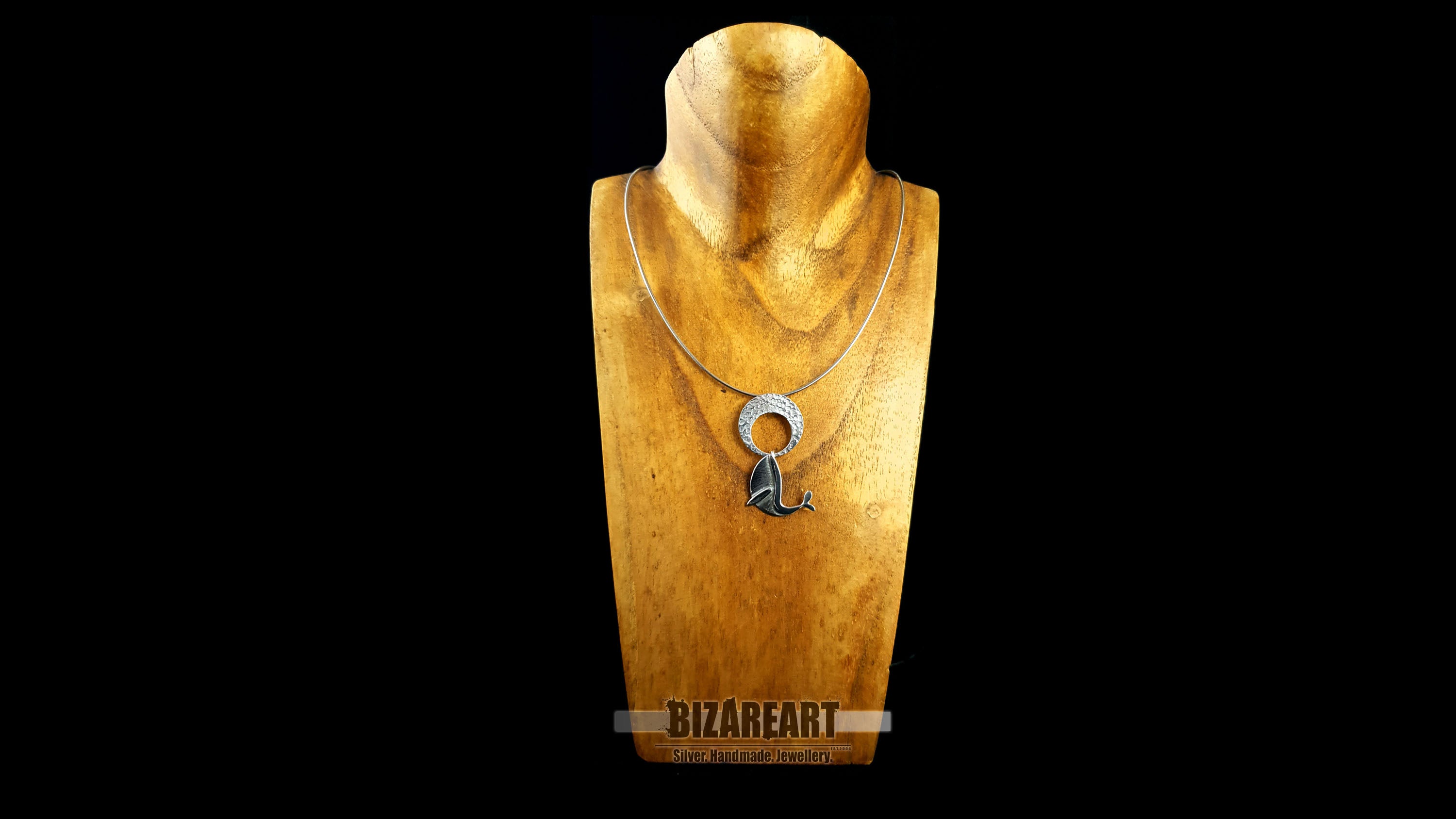 The handmade silver whale pendant worn on a silver chain layered on a gold mannequin bust, demonstrating how the kinetic necklace hangs seamlessly and styles with modern fashion.