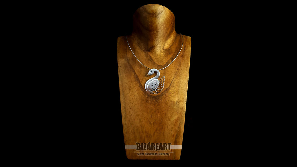 The handcrafted swan pendant styled on a silver chain over a wooden jewelry mannequin to show how it hangs when worn.
