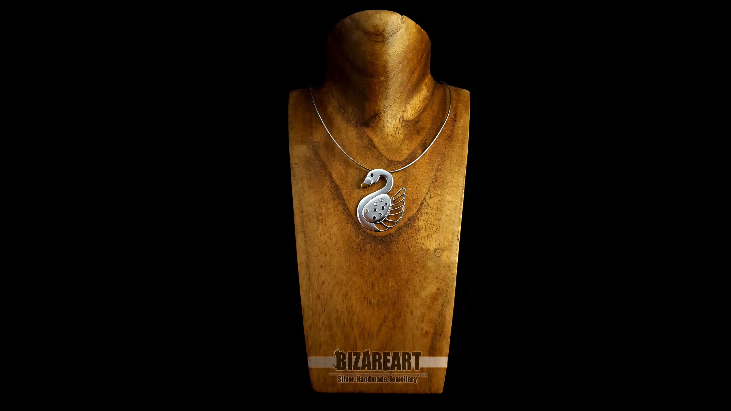 The handcrafted swan pendant styled on a silver chain over a wooden jewelry mannequin to show how it hangs when worn.