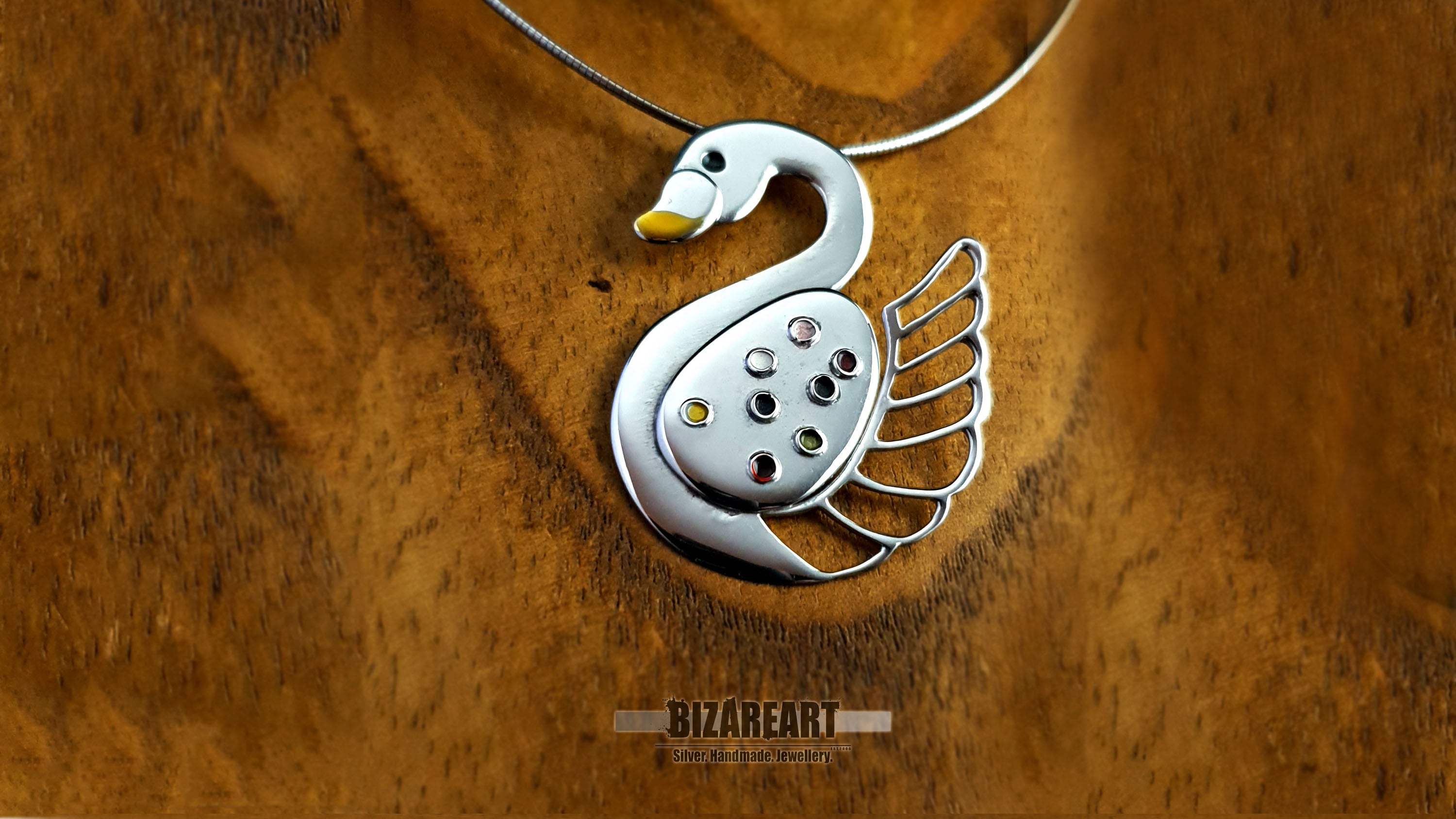Silver swan pendant resting on a textured wooden surface, showcasing the warm reflections and artisan craftsmanship.