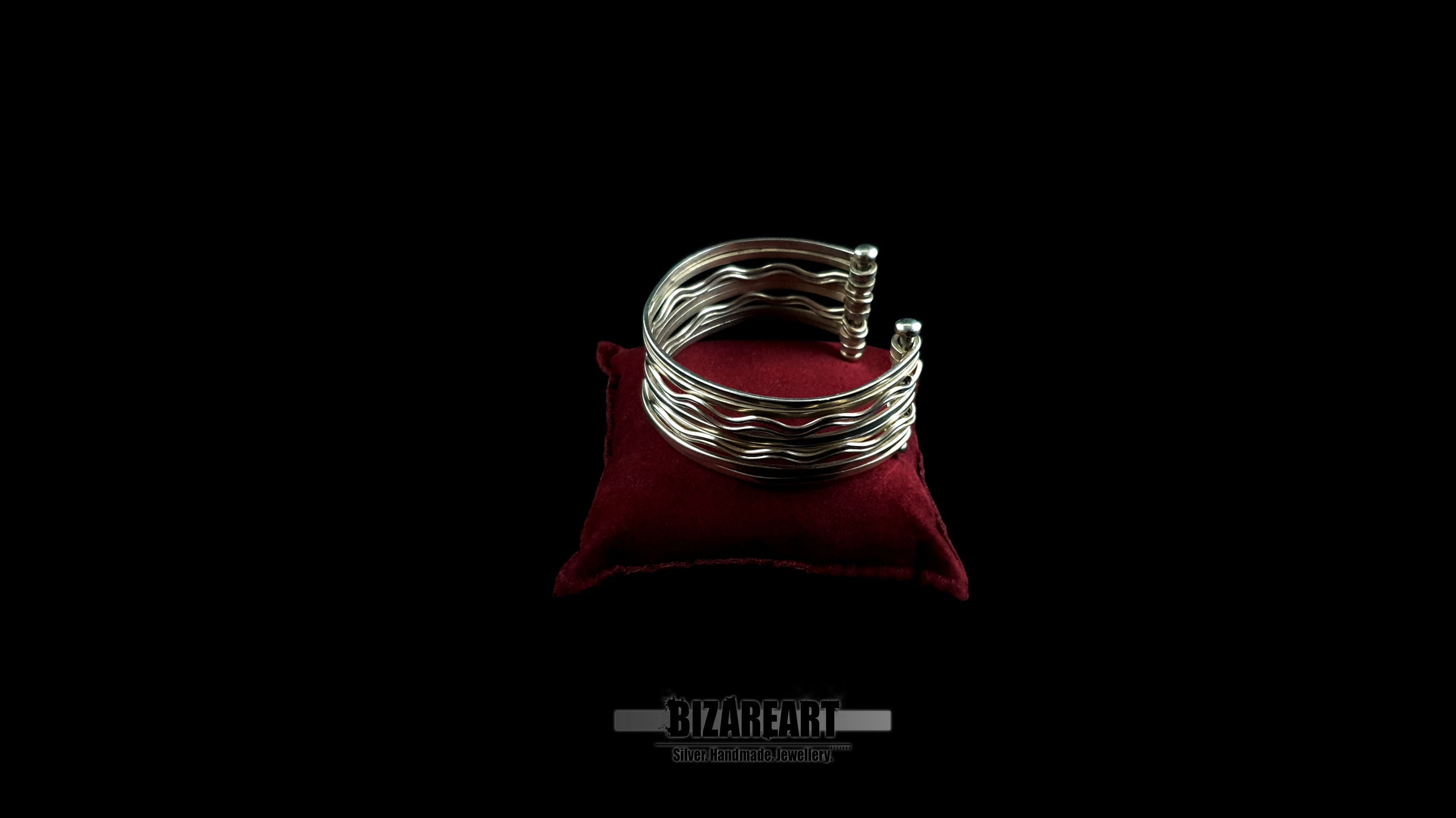 Fully handmade 10-strand sterling silver wave cuff bracelet with high-reflectivity mirror finish displayed on a red velvet jewelry pillow.