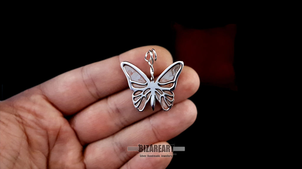 hand held view of the Bizareart butterfly pendant held between fingers to demonstrate the 3.4cm scale and artisan detail.