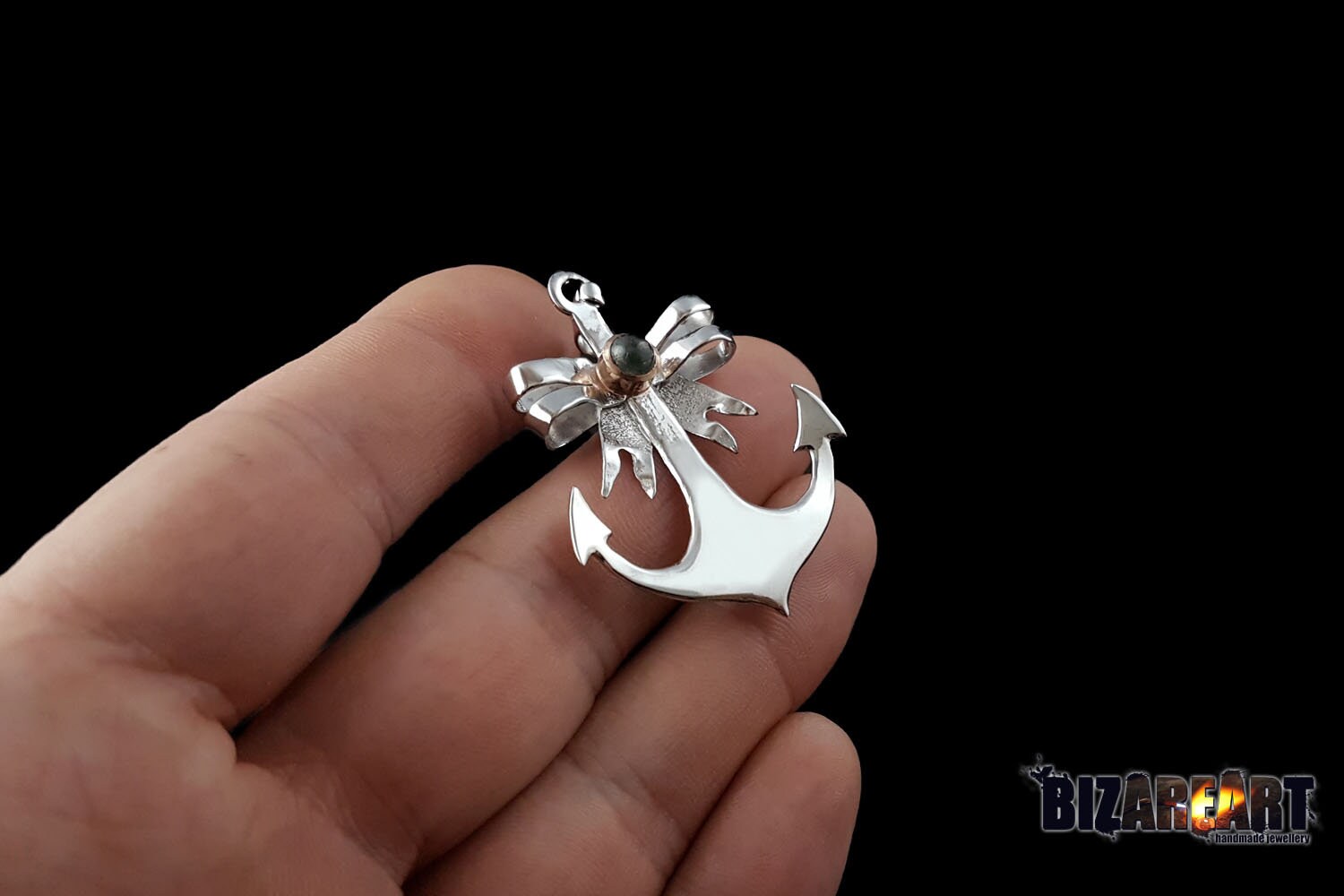 The anchor pendant held between two fingers to provide a clear sense of scale, demonstrating its substantial 8-gram weight and physical dimensions.