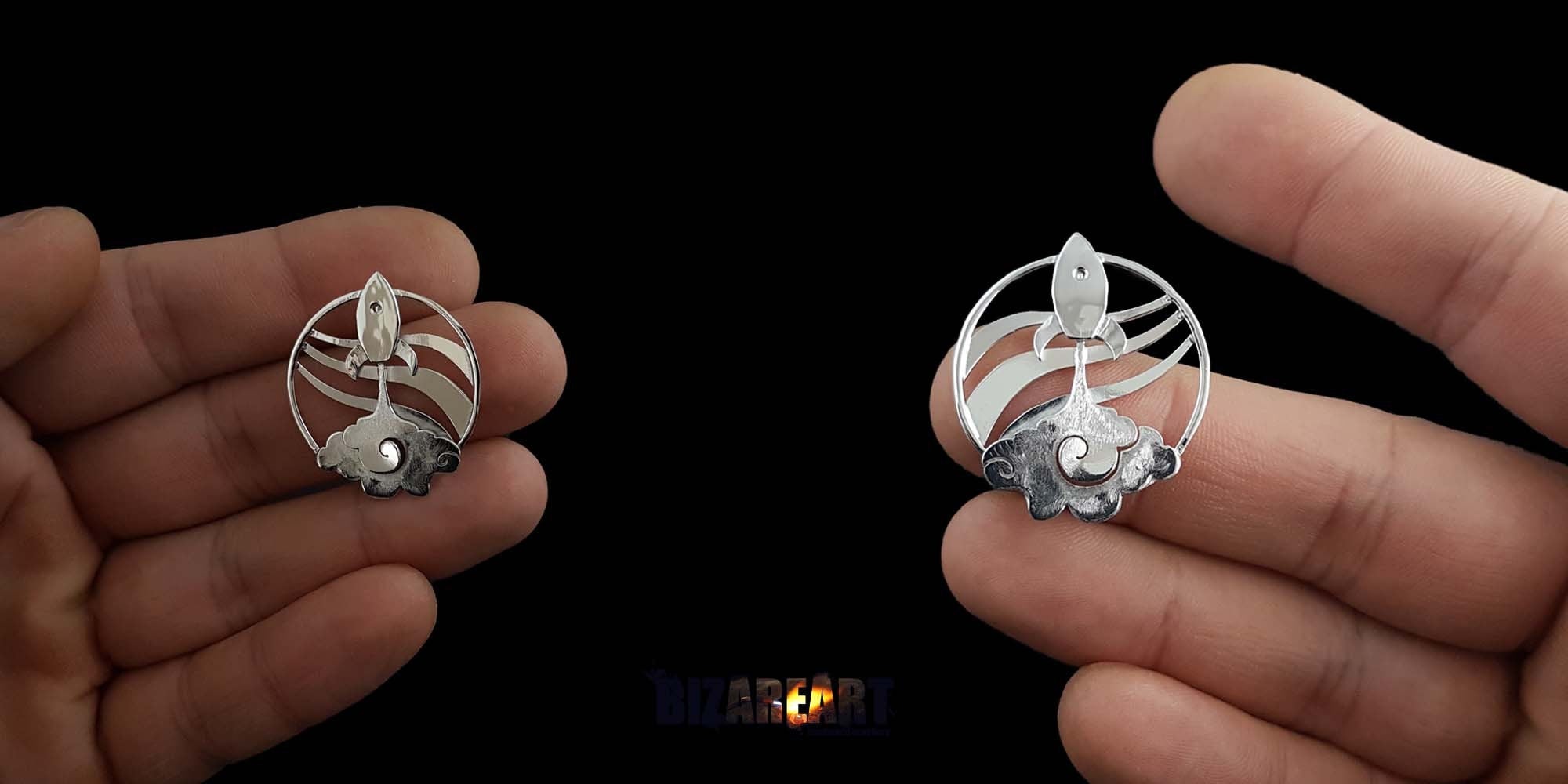 A person holding two Rocket Necklace V2.0 pendants between their fingers to demonstrate the actual size, scale, and high-shine rhodium finish.