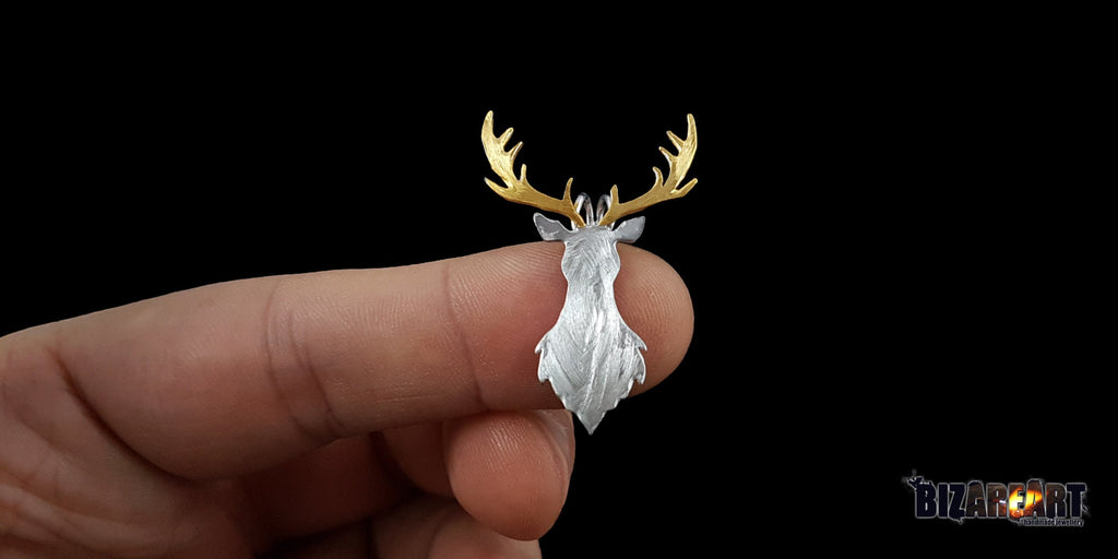 A person holding the deer pendant between their thumb and forefinger to demonstrate its true size and 4.0 cm height relative to a hand.