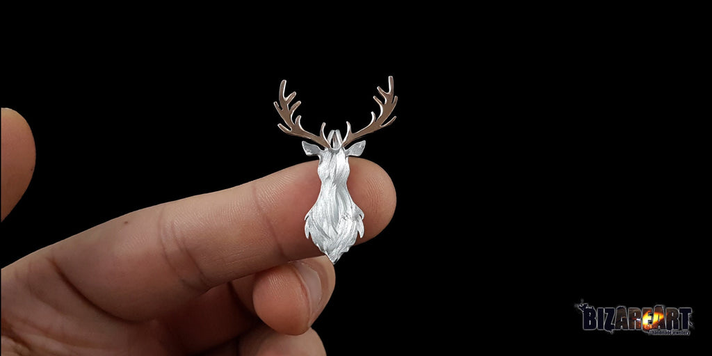 A scale-reference shot showing the deer pendant held between two fingers, demonstrating its delicate size and detailed craftsmanship relative to a person's hand.