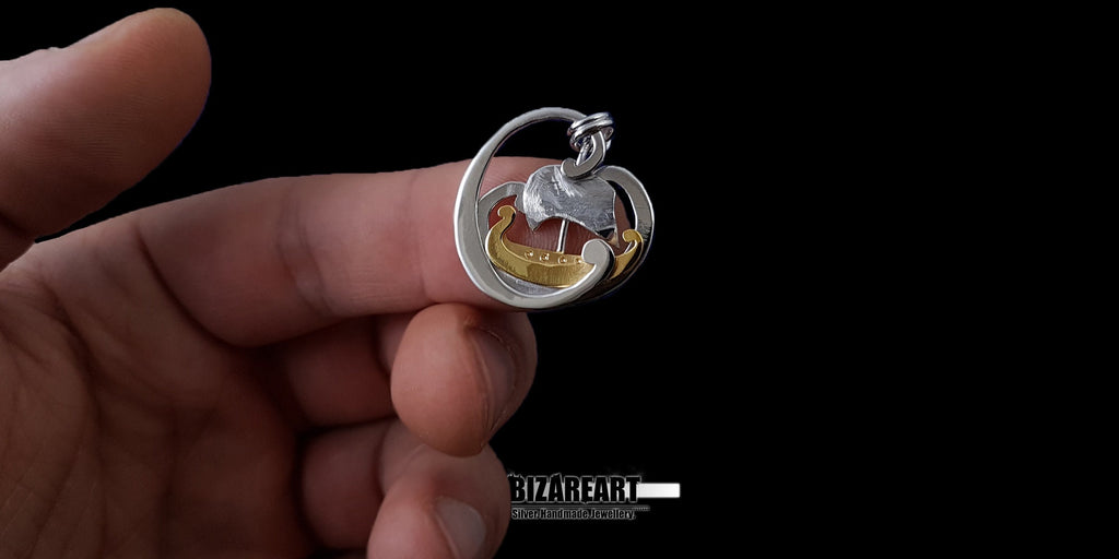 A hand holding the Tiny Boat Pendant between two fingers to demonstrate the small, delicate scale and the craftsmanship of the piece.