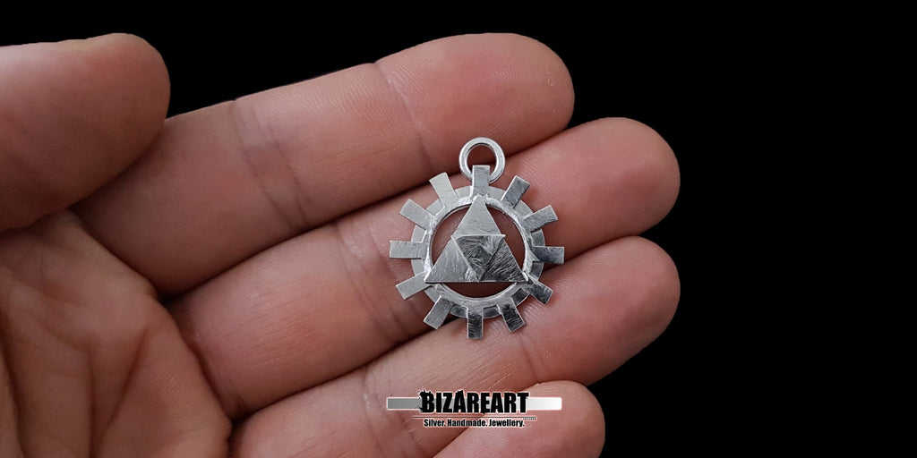 The sterling silver Triforce pendant resting flat on an open palm, providing a clear visual reference for its compact size and wearable dimensions.