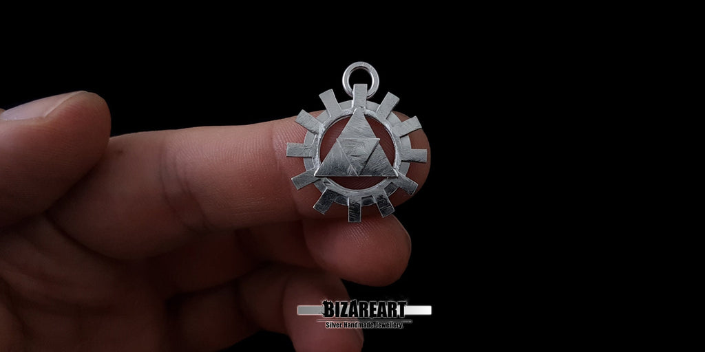 A hand holding the silver Triforce gear pendant between fingers to demonstrate its real-world size, scale, and high-quality craftsmanship.