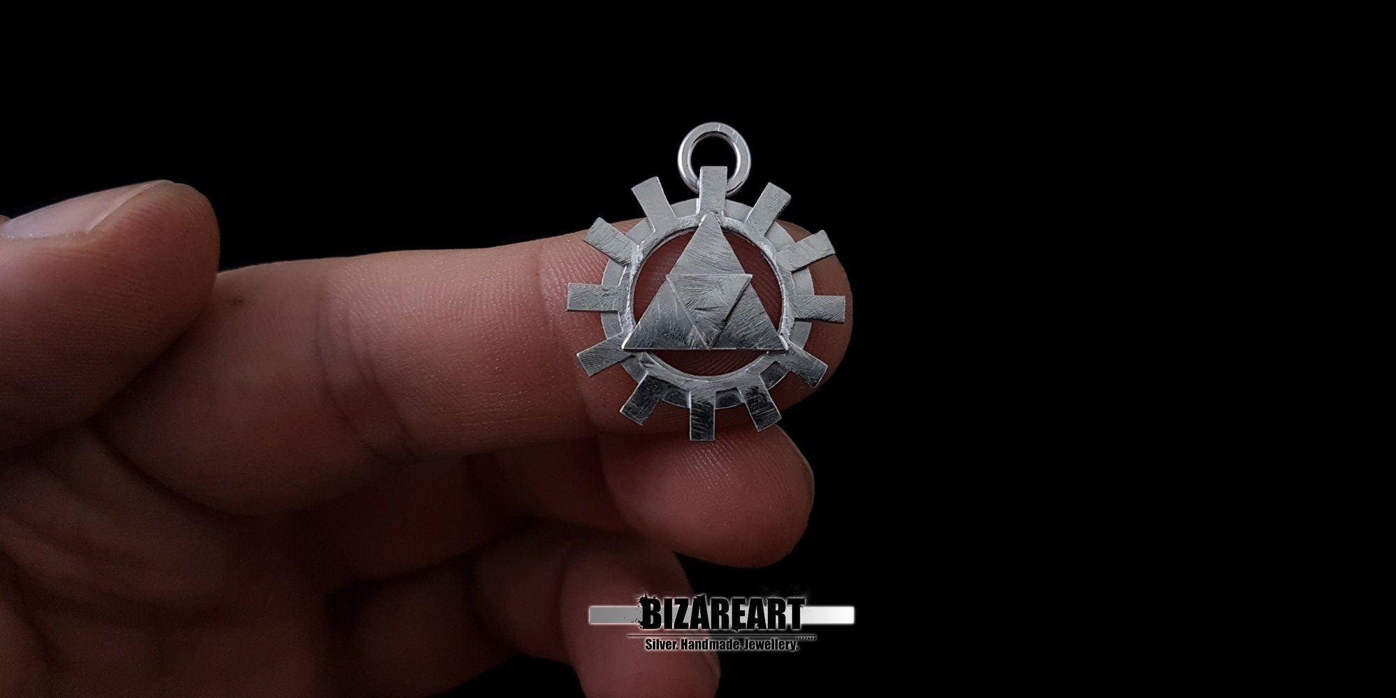 A hand holding the silver Triforce gear pendant between fingers to demonstrate its real-world size, scale, and high-quality craftsmanship.
