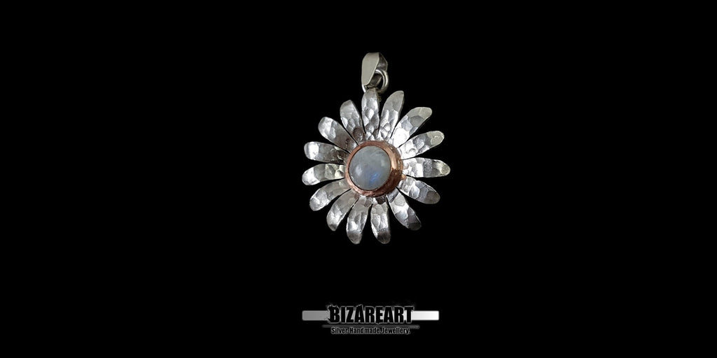 Close-up of a handcrafted 925 sterling silver flower pendant with a central moonstone cabochon, highlighting the rustic, raw texture of the background finish.
