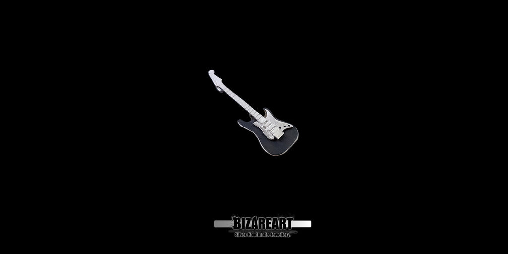 A three-quarter angled view of the guitar pendant, displaying the sculptural depth, carved edges, and the secure silver wire hanger at the headstock.