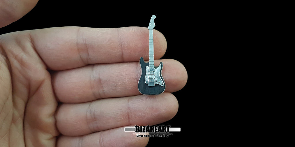 A guitar pendant held in a person's palm to show scale, illustrating the delicate miniature size and handcrafted detail of the jewelry.