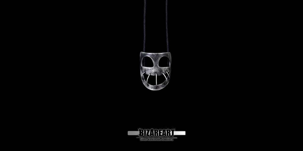 Distant, minimal shot highlighting the eerie, dark elegance of the small silver mask necklace against a black backdrop.