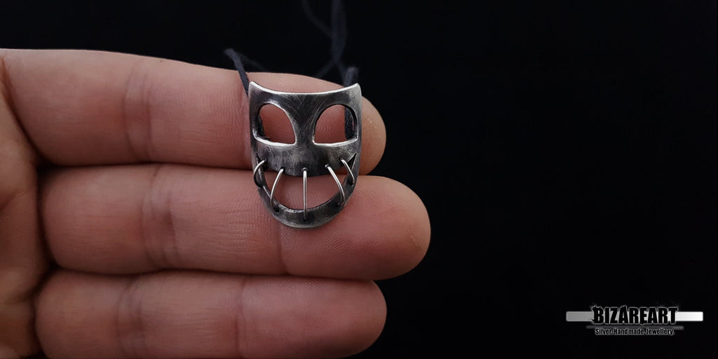 Scale demonstration showing a hand holding the 2.5 cm handmade Bizareart silver mask pendant to illustrate its wearable size.