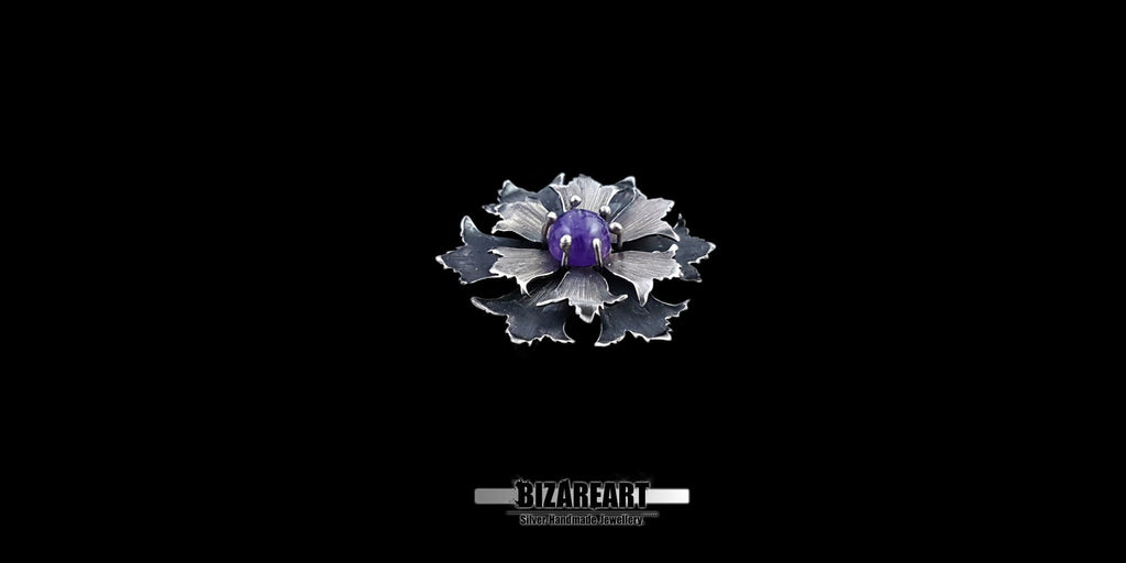 Wide studio shot of a layered sterling silver floral pendant with detailed textured petals and a central purple gemstone against a black background.