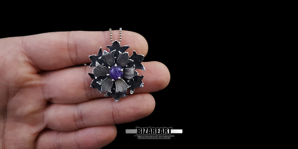 A hand holding the silver flower pendant by its chain, demonstrating how the botanical jewelry piece hangs and looks when worn.