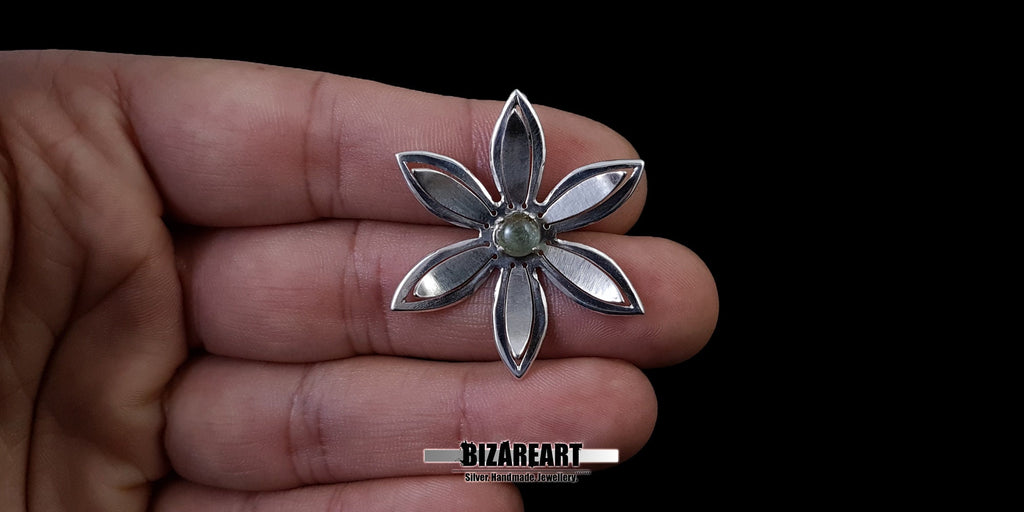 A person holding the silver flower pendant in the palm of their hand to demonstrate its physical size and scale relative to a human hand.