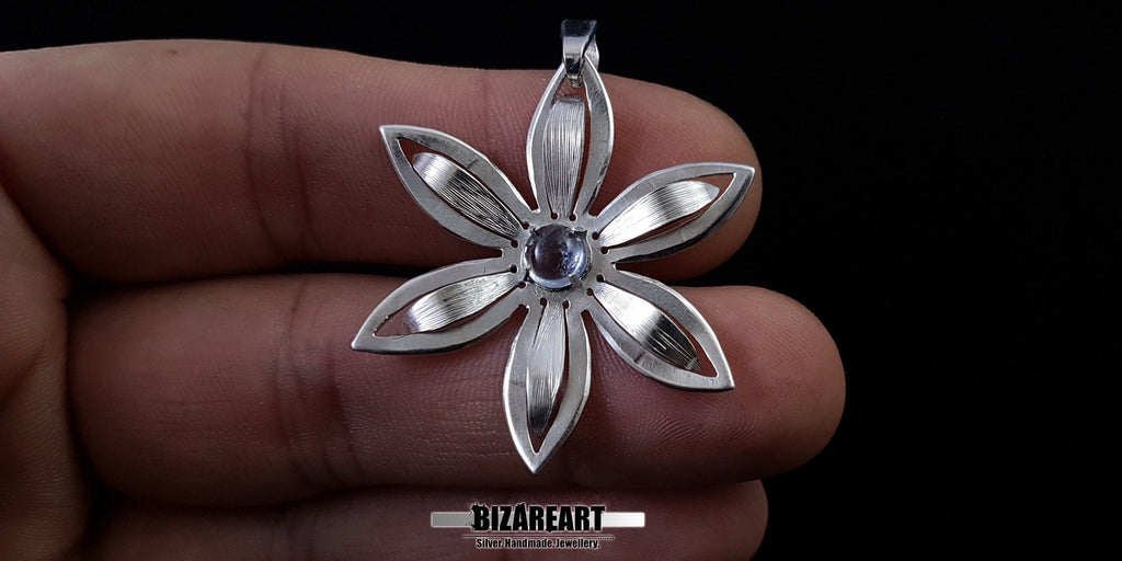 Handcrafted silver flower pendant held in hand to demonstrate the 4cm size and scale.