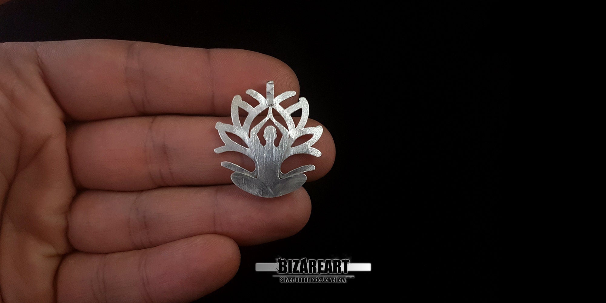 A lifestyle close-up of the pendant being held between two fingers to provide a clear scale of its size and the depth of the carved silver edges.
