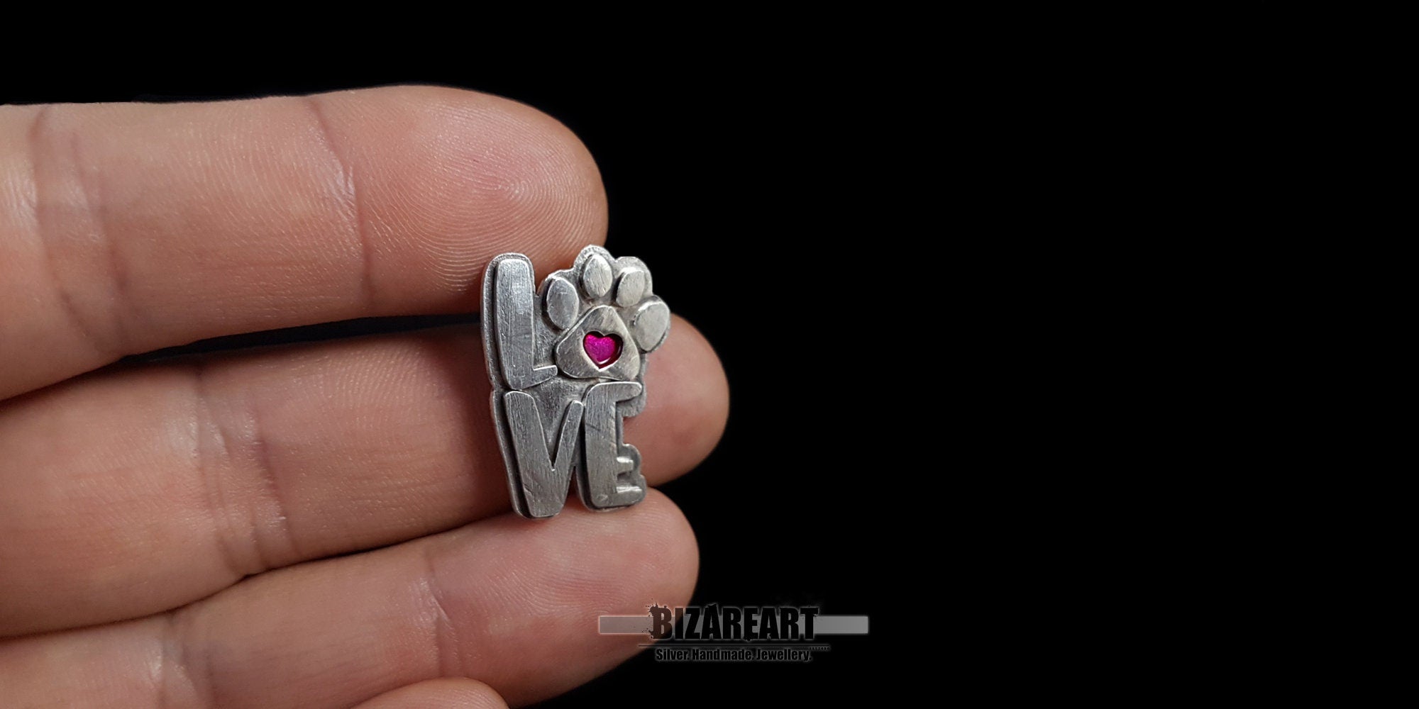 A person holding the small silver pendant between their fingers to demonstrate its actual size and portable, lightweight design.