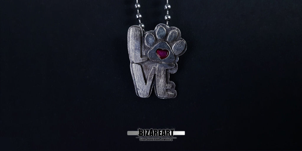 The silver "LOVE" paw pendant hanging from a delicate silver ball chain, highlighting its scale and how the magenta heart pops against the metallic finish.