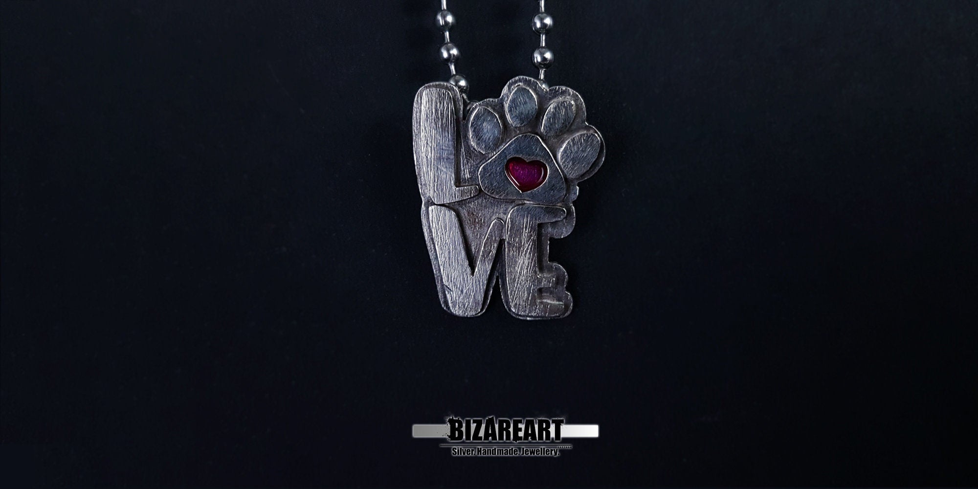 The silver "LOVE" paw pendant hanging from a delicate silver ball chain, highlighting its scale and how the magenta heart pops against the metallic finish.