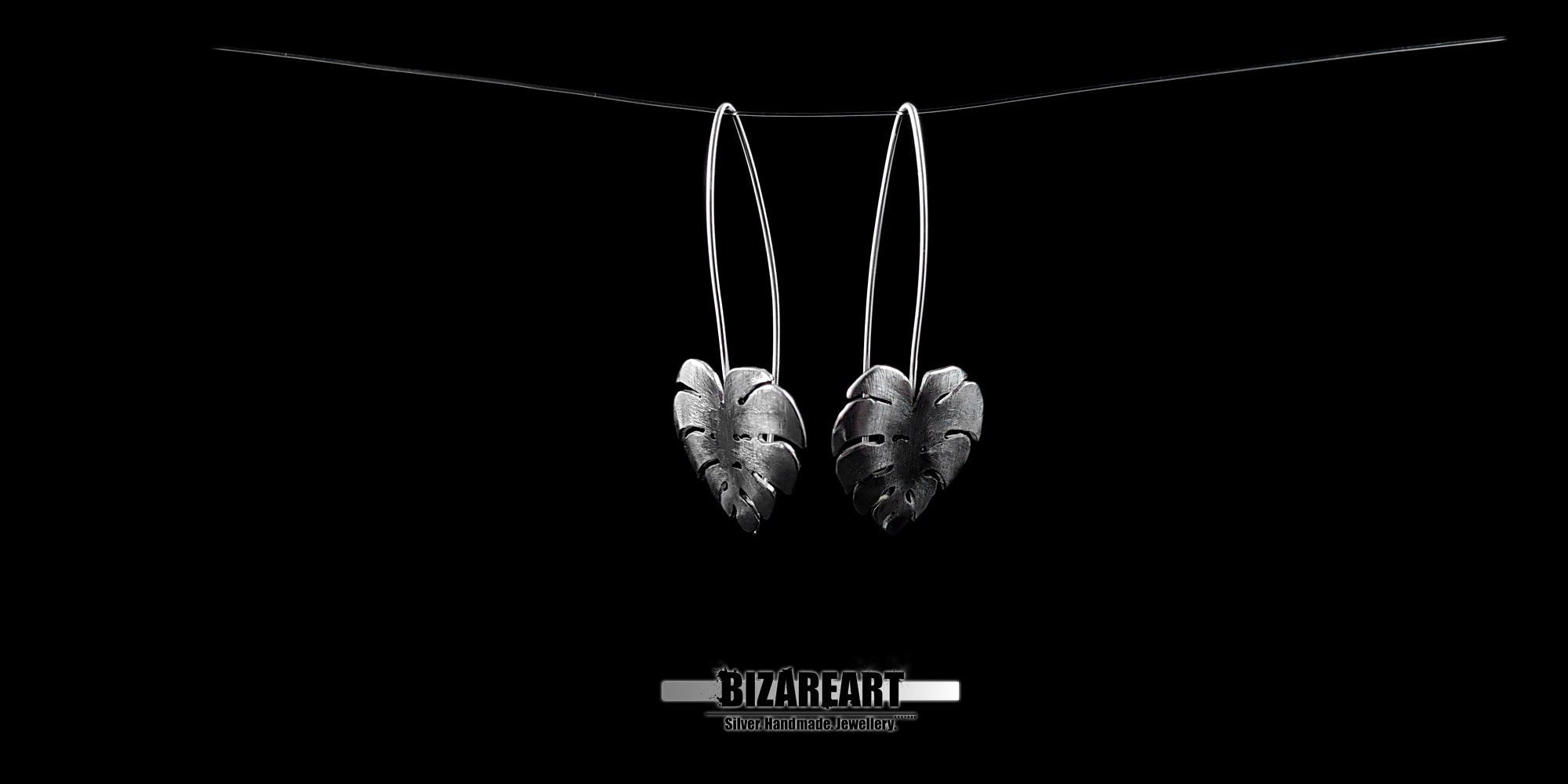 Two sterling silver tropical leaf earrings hanging side-by-side, emphasizing the lightweight design and potential for natural movement.