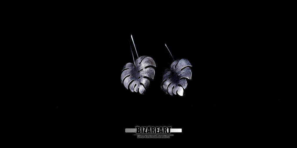 Side-profile view of handcrafted 925 silver Monstera leaf earrings featuring intricate vein detailing and antique oxidation against a black background.