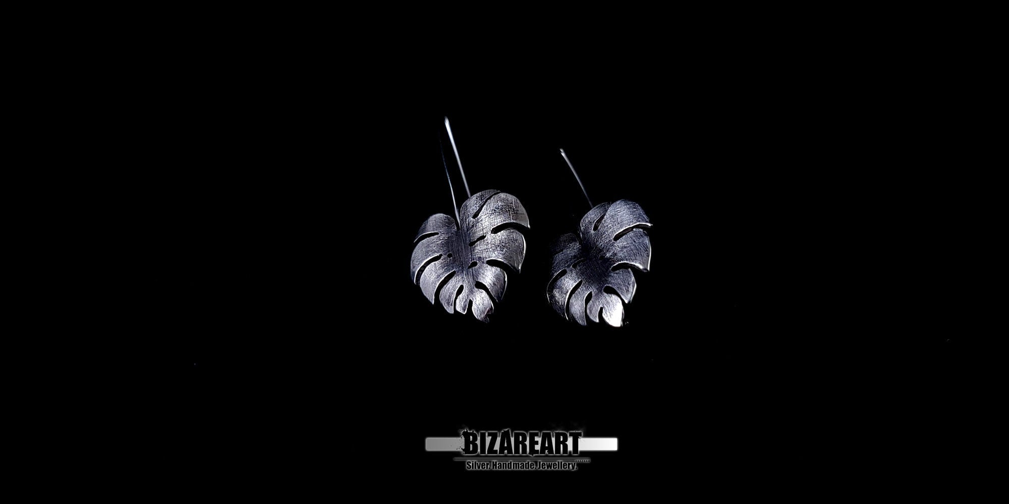 Side-profile view of handcrafted 925 silver Monstera leaf earrings featuring intricate vein detailing and antique oxidation against a black background.
