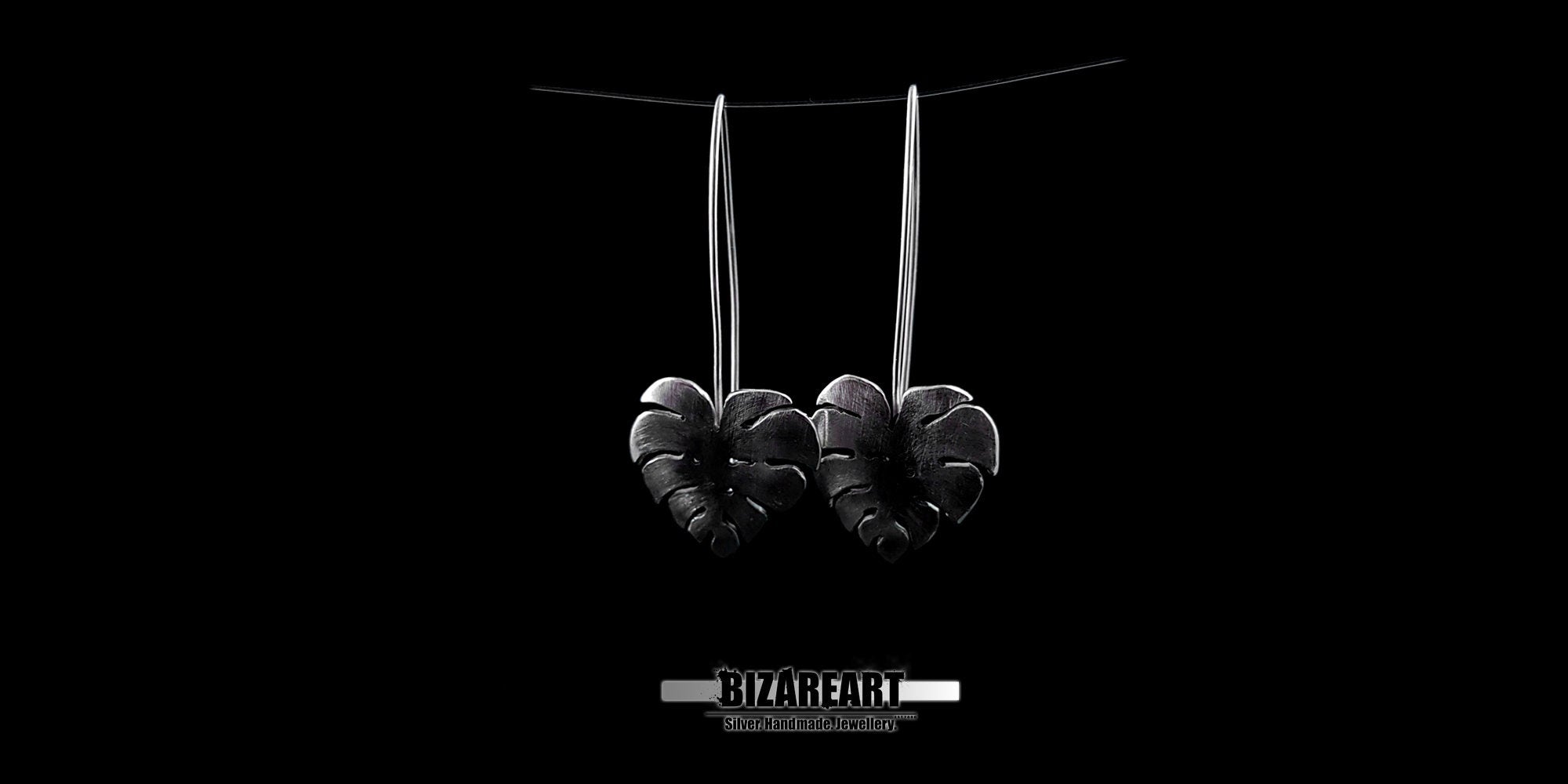 Monstera leaf earrings held in a hand to demonstrate the true size and proportions of the 6.2g solid silver pieces.