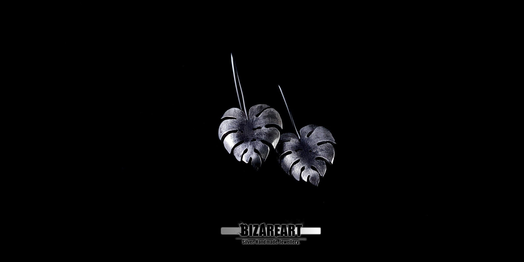 Detailed shot of the Monstera earrings highlighting the contrast between the shiny carved outlines and the grainy, oxidized background.