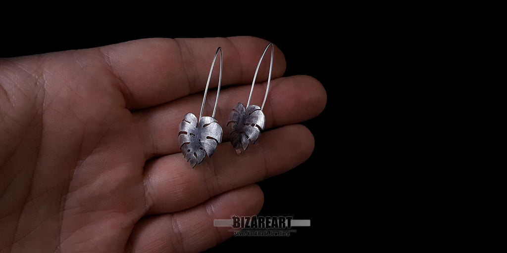 Monstera leaf earrings held in a hand to demonstrate the true size and proportions of the 6.2g solid silver pieces.