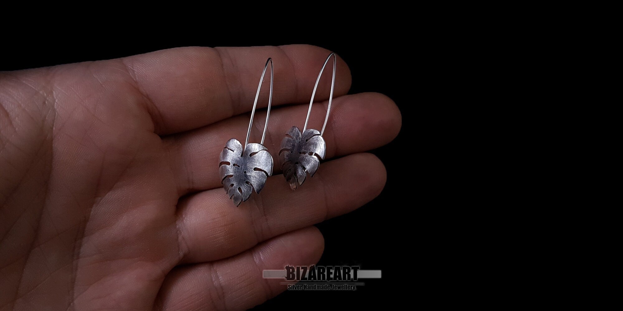 Monstera leaf earrings held in a hand to demonstrate the true size and proportions of the 6.2g solid silver pieces.