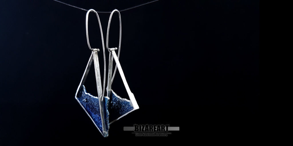 Close-up of the ocean-inspired silver earrings showing the reflective, light-catching qualities of the blue enamel and silver trim.