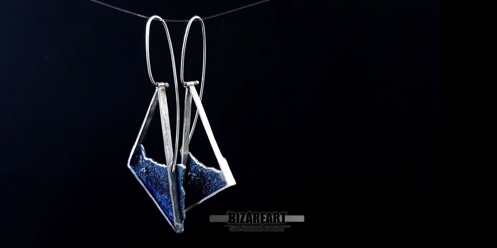 Close-up of the ocean-inspired silver earrings showing the reflective, light-catching qualities of the blue enamel and silver trim.