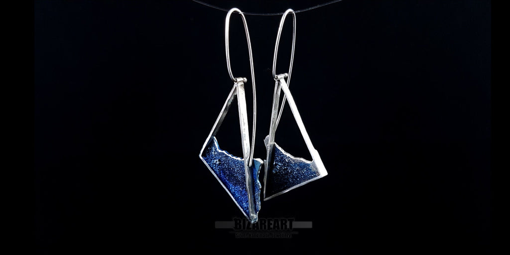 Asymmetrical sterling silver beach-inspired dangle earrings with deep blue liquid enamel and long wire hooks on a black background.