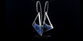 Asymmetrical sterling silver beach-inspired dangle earrings with deep blue liquid enamel and long wire hooks on a black background.
