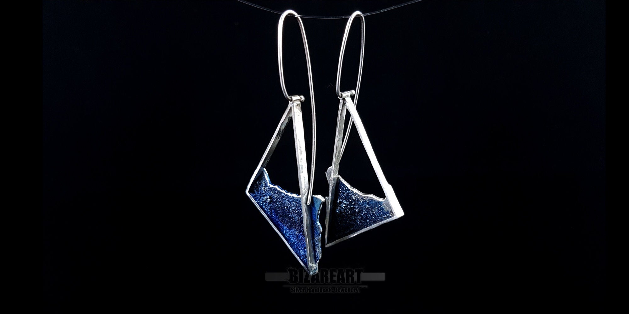 Asymmetrical sterling silver beach-inspired dangle earrings with deep blue liquid enamel and long wire hooks on a black background.