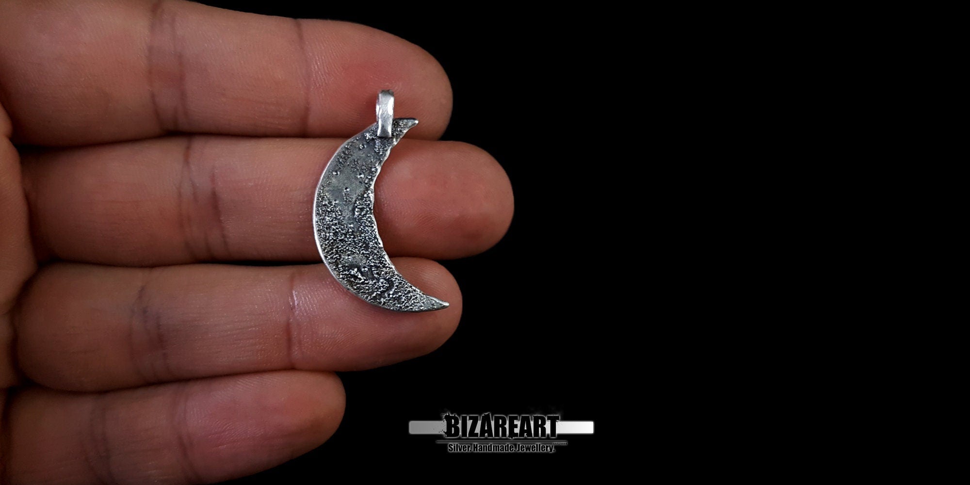 Silver crescent moon pendant held between fingers to show its small size.