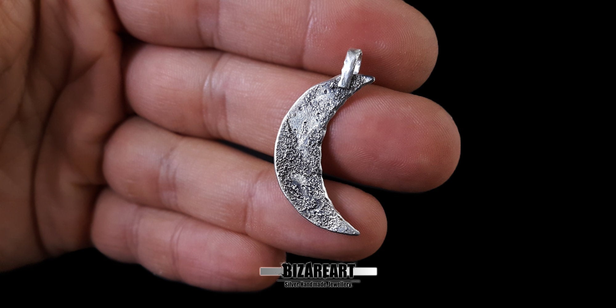 Textured silver crescent moon pendant lying flat in an open hand for scale.