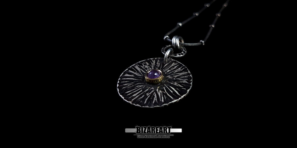Dramatic low-angle shot of the Bromo Charm on a black background, emphasizing the bronze crater and the depth of the amethyst gemstone.