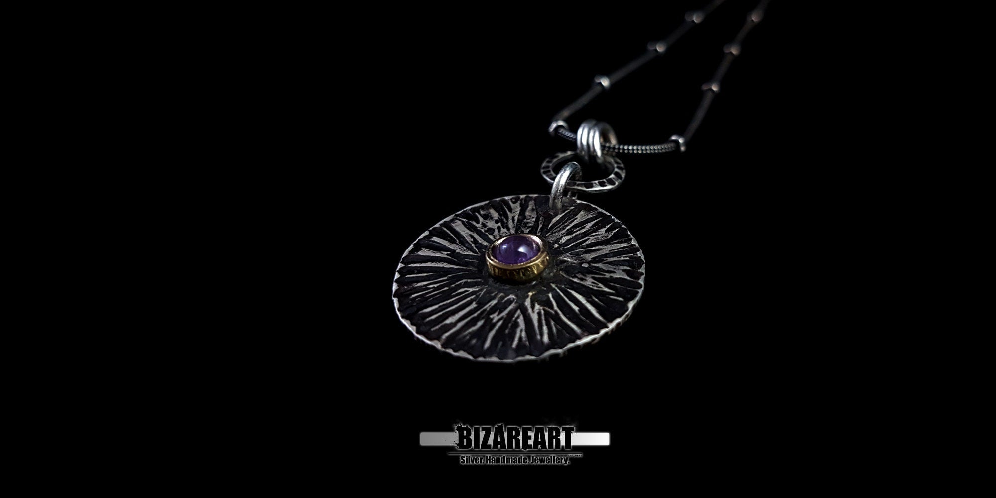 Dramatic low-angle shot of the Bromo Charm on a black background, emphasizing the bronze crater and the depth of the amethyst gemstone.